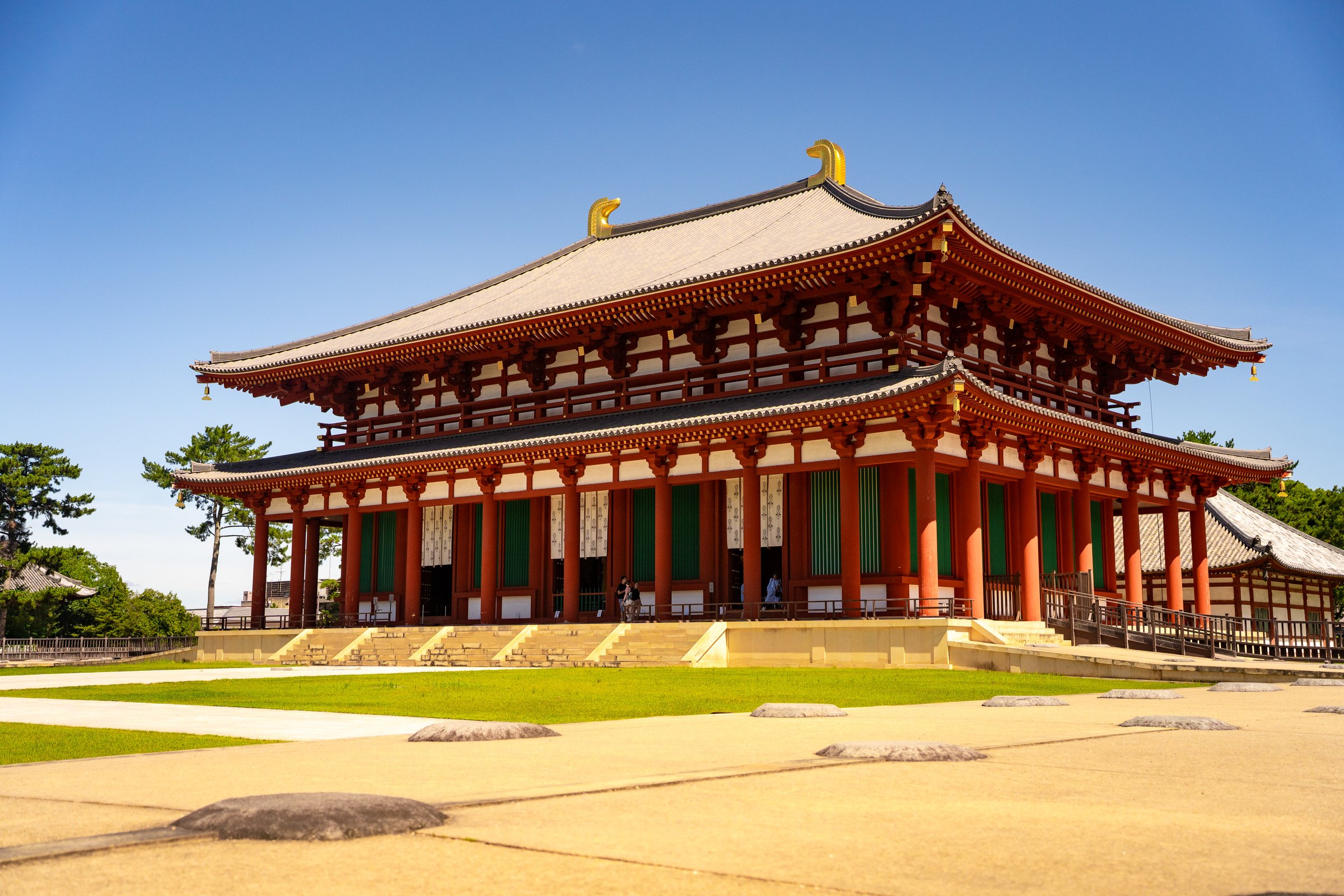 Grand traditional Japanese temple hall with red and green pillars against blue sky